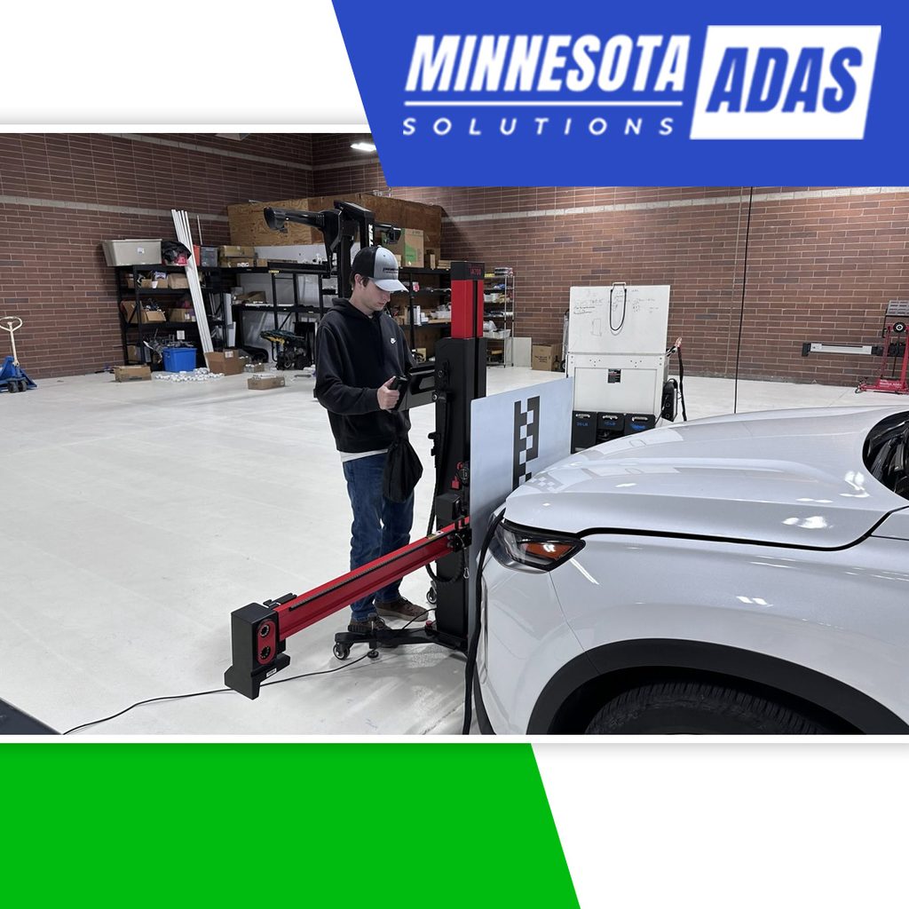 A technician positioning an ADAS calibration target stand and camera sensor directly in front of a white SUV in a repair shop.